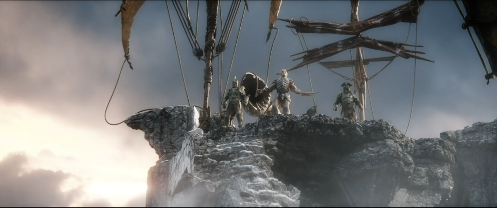 An image of an orc from The Hobbit: The Battle Of Five Armies. There's three orcs, standing on a cliff; we're looking at them from below. The orcs are small and heavily armoured.